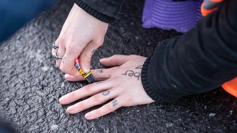 Eine Hand wird mit Sekundenkleber auf eine Straße geklebt.