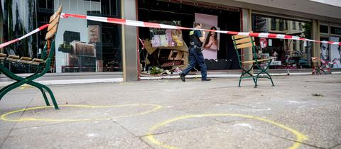 Bürgersteig mit gelben Markierungen auf dem Boden und einem Absperrband der Polizei. Ein Polizist geht darin.
