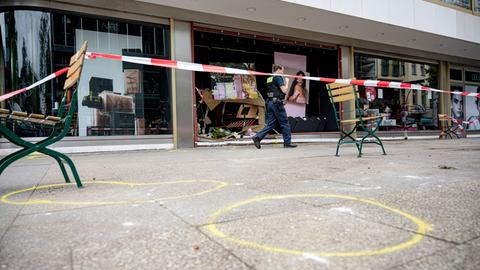 Bürgersteig mit gelben Markierungen auf dem Boden und einem Absperrband der Polizei. Ein Polizist geht darin.