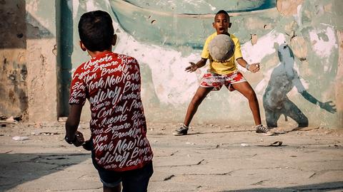 Zwei Jungen stehen sich gegenüber, der eine ist kurz davor, einen Fußball zu fangen, den der andere in seine Richtung geschossen hat.