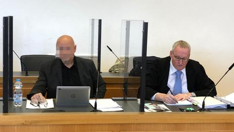 Links sitzt hinter einem Laptop der Angeklagte, rechts neben ihm mit blauer Krawatte sein Anwalt.