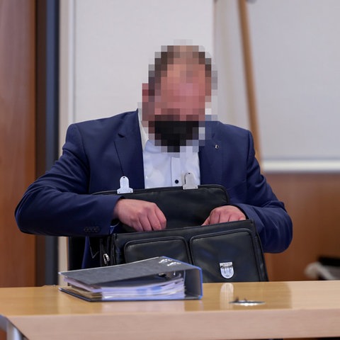 Ein Mann im Anzug sitzt an einem Tisch und legt Dokumente in eine Aktentasche