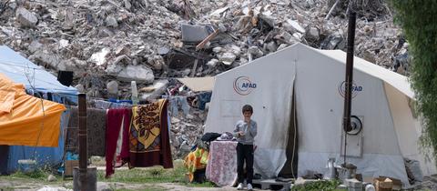 Der neunjährige Yakup steht am Stadtrand von Antakya vor seinem Zelt, in dem er seit dem Erdbeben lebt.