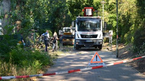 Hinter einer Polizeiabsperrung steht ein aufgebockter Lkw in einem Wohngebiet zwischen Bäumen.