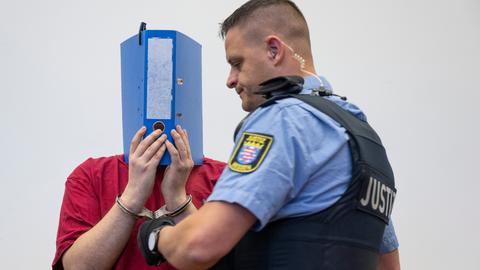Der Angeklagte im Ayleen-Prozess in Gießen verdeckt sein Gesicht mit einem Aktenordner.