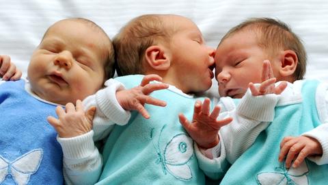 Drei Babys liegen nebeneinander auf einer weißen Decke.