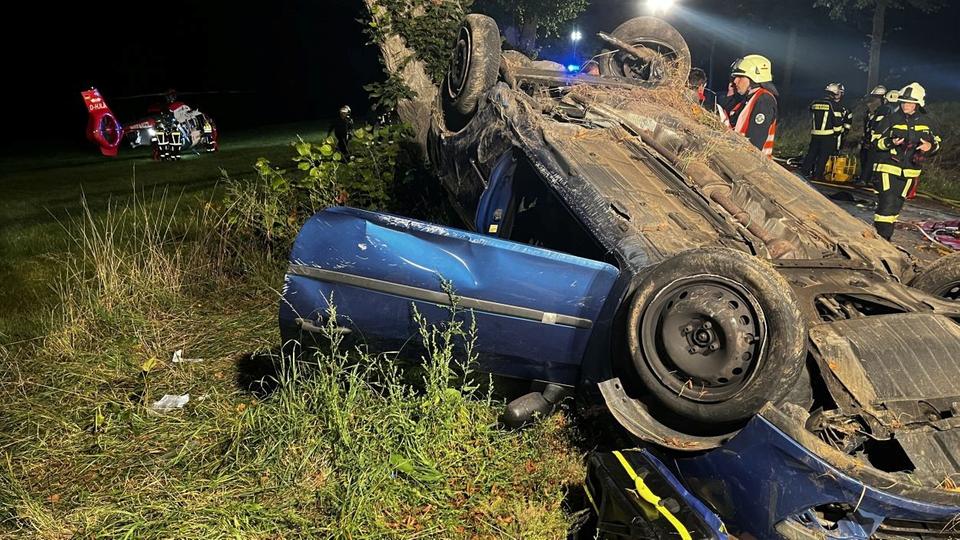 Auto liegt auf dem Dach, Rettungskräfte und Hubschrauber im Hintergrund