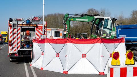 Am Rand einer Straße stehen ein Rettungswagen und ein Sichtschutz. Dahinter ist der obere Teil des Unfall-Bagger zu sehen.