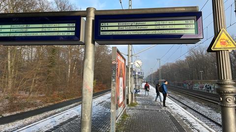 Ein leicht verschneiter Bahnsteig, drauf stehen im Hintergrund drei Menschen. Eine Anzeigetafel ist zu sehen, auf der diverse Zugausfälle angekündigt werden.
