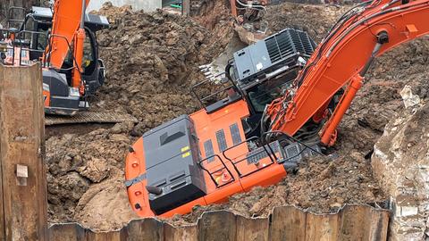 Ein orangener Bagger hat sich in dem aufgeweichten Erdreich festgefahren.