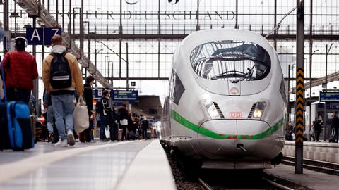 Passagiere mit Gepäck auf einem Bahnsteig an einem Gleis, auf dem ein ICE steht.