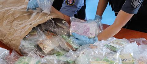 Polizisten schütten einen Sack mit Geld in Tüten auf einen Tisch