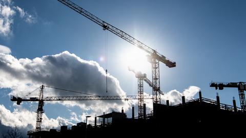 Hinter den Baukränen an einer Baustelle scheint die Sonne.