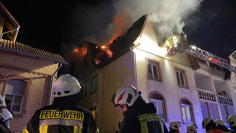 Feuerwehrmänner stehen vor einem Haus, bei dem es im dritten Stock brennt