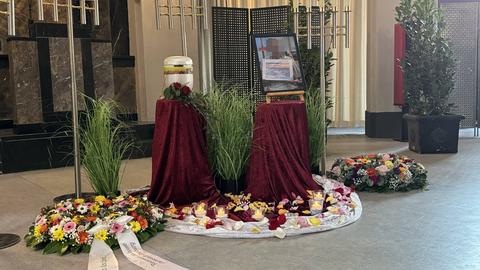 Blumen und Kränze liegen vor einer Urne in der Trauerhalle.