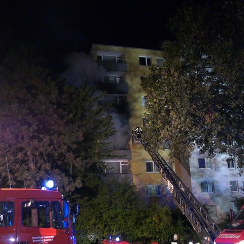 Feuerwehrwagen stehen vor einem Haus, aus dessen Fenstern dichter Rauch zeiht