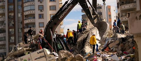 Ein Bagger und mehrere Helfer stehen auf einem Berg aus Schutt. 