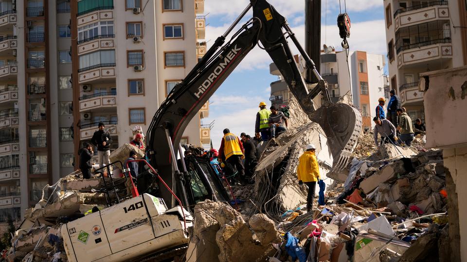 Ein Bagger und mehrere Helfer stehen auf einem Berg aus Schutt. 