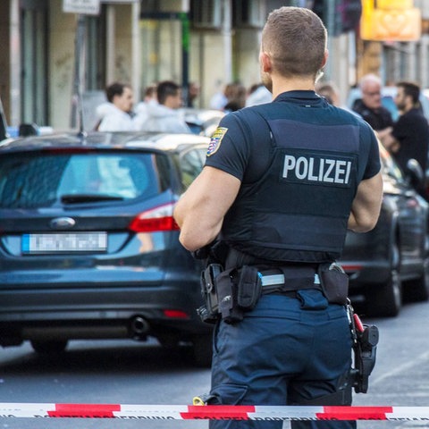 Polizist im Vordergrund, Flatterband und Autos und weiter Polizisten unscharf im Hintergrund