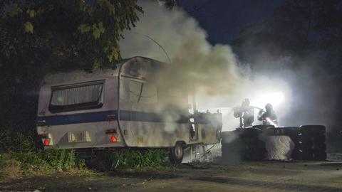 Feuerwehrleute löschen brennenden Wohnwagen, Rauch steigt daraus auf