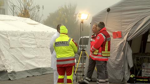 Mehrere Rettungssanitäter und Ärzte stehen vor großen weißen Zelten.