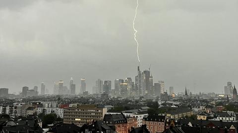 Blick auf eine Skyline mit Hochhäusern unter/vor einem sehr grauen Himmel. Ein zackige Blitzlinie führt vom oberen Bildrand direkt auf ein Hochhaus.