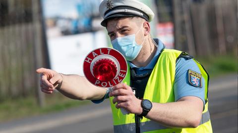 Ein Polizist hält eine Kelle mit der Aufschrift "Halt Polizei" und zeigt mit dem Finger in Richtung des Fotografierenden.