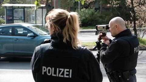 Zwei Polizisten mit einem mobilen Blitzer, dahinter ein Auto