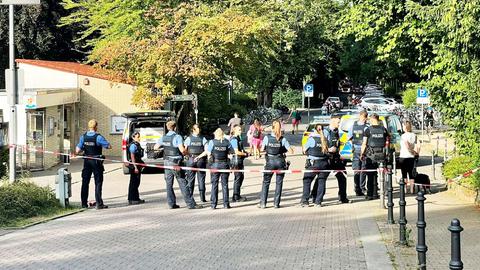 Einsatzkräfte der Polizei auf einer Straße hinter einem Absperrband.