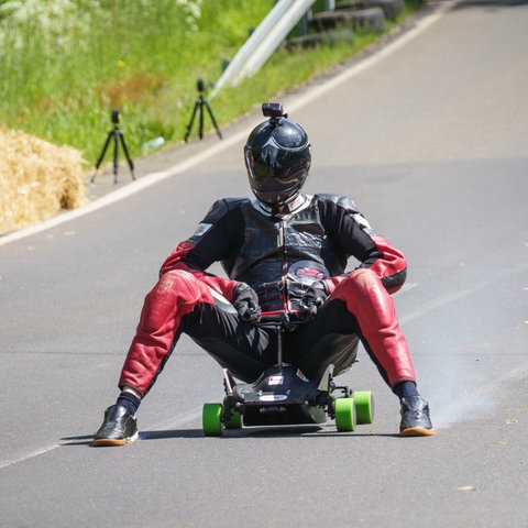 Ein fährt auf einem Bobbycar eine Straße hinunter.