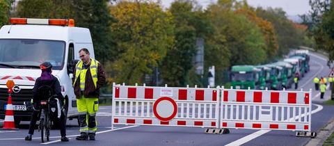 Ein Sicherheitsmitarbeiter steht an einer Straßenabsperrung auf einer Straße, auf dem Schild an der Absperrung steht "Achtung, Bombenentschärfung!"