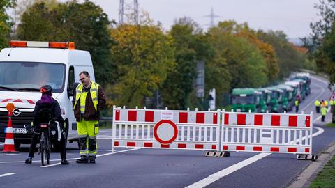 Ein Sicherheitsmitarbeiter steht an einer Straßenabsperrung auf einer Straße, auf dem Schild an der Absperrung steht "Achtung, Bombenentschärfung!"