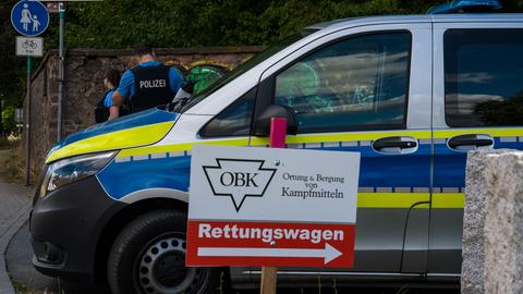 Auf einem Schild steht "Ortung und Bergung von Kampfmitteln", daneben ein Polizeiauto.