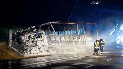 Zwei Feuerwehrleute stehen im Dunkeln vor dem Gerippe eines ausgebrannten LKWs.
