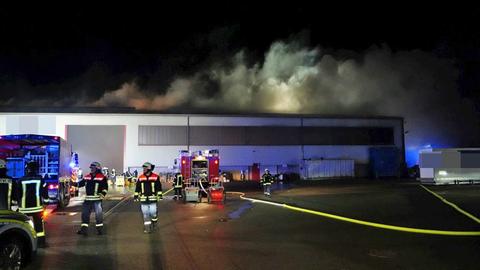 Feuerwehrleute vor einer Halle, aus der Rauch steigt.