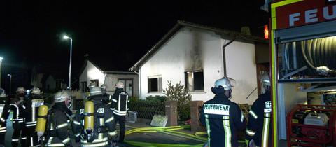 Feuerwehrleute stehen im Dunkeln vor einem Haus mit Brandspuren