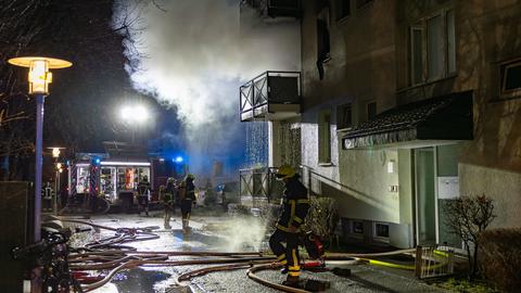 Feuerwehrkräfte in der Nacht vor dem Haus, Rauch quillt aus einer Wohnung, Löschwasser tropft von den Balkonen