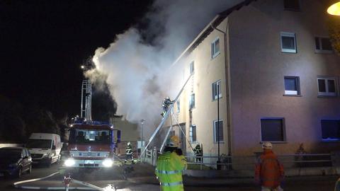 Feuerwehrmann steht auf einer Leiter, weißer Rauch kommt aus dem Haus