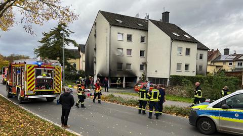 Feuerwehrautos stehen vor einem Mehrfamilienhaus, das von außen voller Ruß ist.