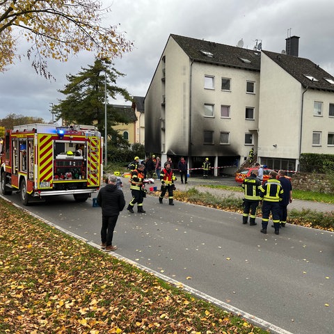 Feuerwehrautos stehen vor einem Mehrfamilienhaus, das von außen voller Ruß ist.