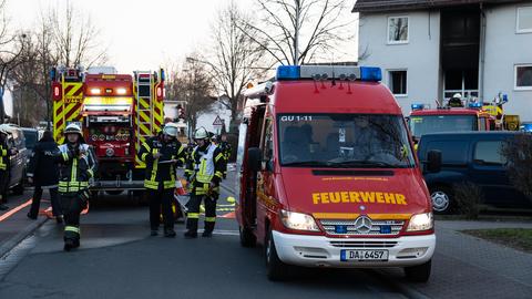 Mehrere Feuerwehrautos stehen in einer Wohnstraße, dahinter ist ein Haus mit Ruß an der Fassade zu sehen.