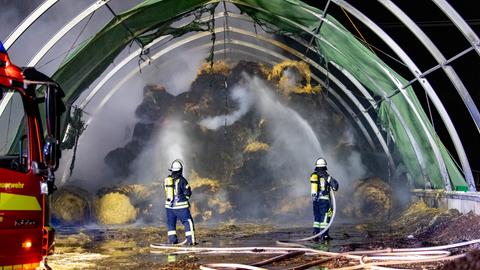 Die Feuerwehr löscht die in Brand geratenen Rundballen.