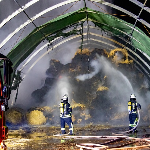 Die Feuerwehr löscht die in Brand geratenen Rundballen.