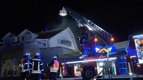 Vor einer Kfz-Werkstatt stehen ein Feuerwehrauto mit ausgefahrener Leiter und mehrere Einsatzkräfte.