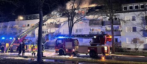 Zwei Feuerwehrautos vor einem Mehrfamilienhaus, aus dessen Dach Rauch aufsteigt