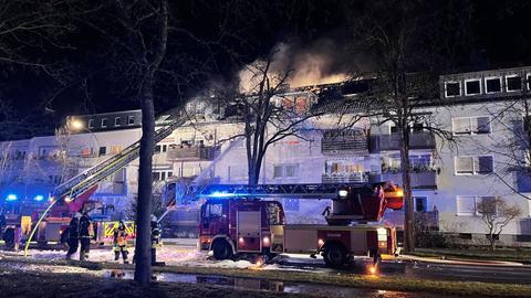 Zwei Feuerwehrautos vor einem Mehrfamilienhaus, aus dessen Dach Rauch aufsteigt