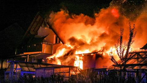 Rauch und Flammen über dem Haus, das sich vor einem pechschwarzen Himmel abzeichnet.