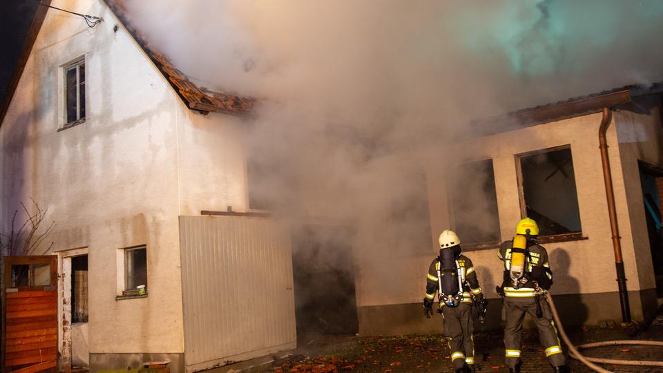 Dicker Rauch dringt aus Gebäude, Feuerwehrleute mit Schlauch