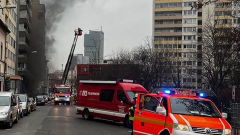 Feuerwehrautos stehen auf einer Straße, im Hintergrund dunkler Rauch.