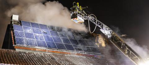 Die Feuerwehr bei Löscharbeiten mit einer Drehleiter an einem Haus mit Solaranlage auf dem Dach, aus dem es raucht.